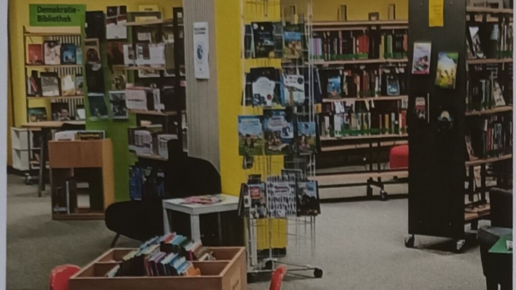 Innenraum einer Bibliothek mit Bücherregalen, Ausstellungstafeln, Sitzmöglichkeiten und Buchauslagen.