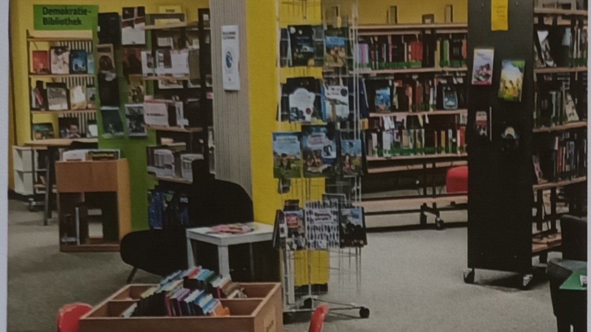 Innenraum einer Bibliothek mit Bücherregalen, Ausstellungstafeln, Sitzmöglichkeiten und Buchauslagen.