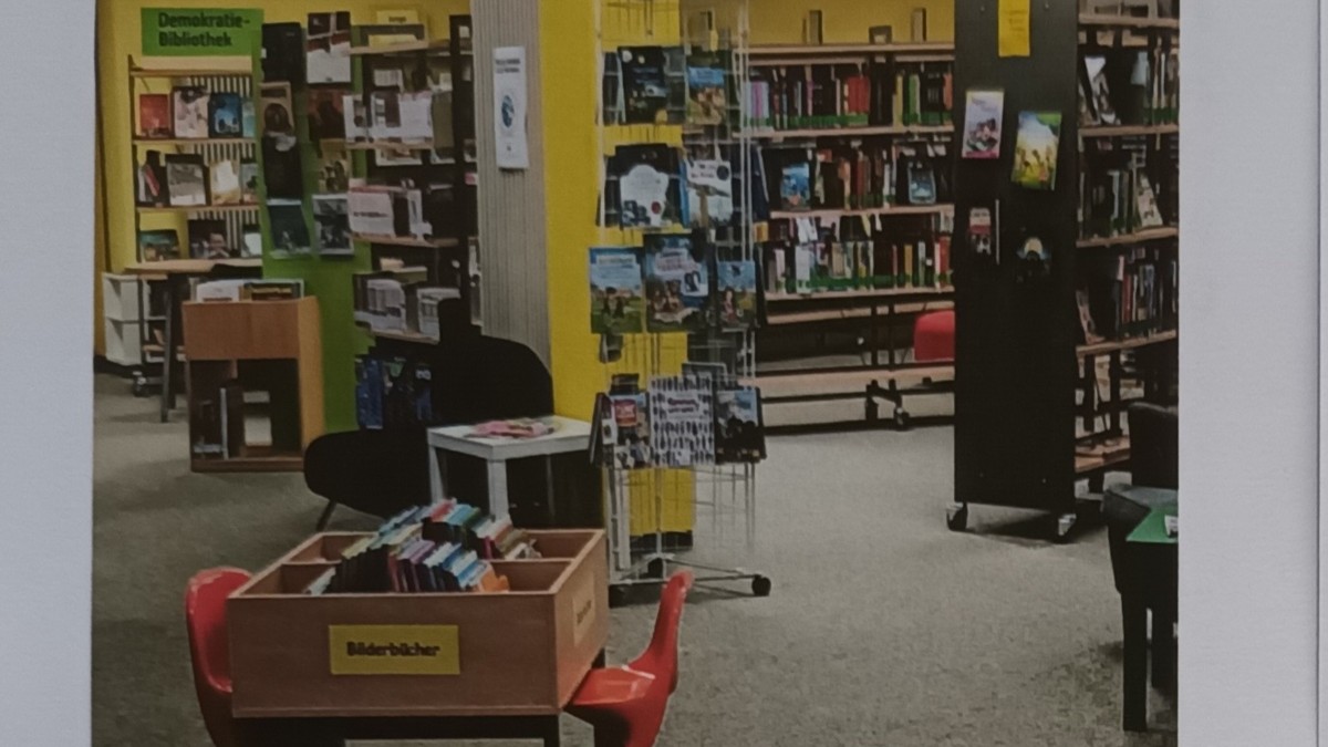 Innenraum einer Bibliothek mit Bücherregalen, Ausleihtheken und gelb-grünen Wandflächen.